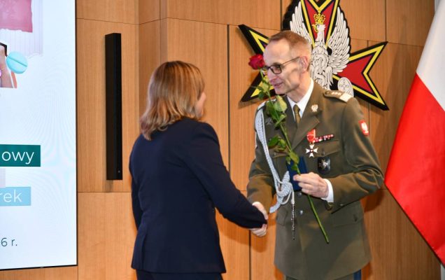 Dyrektor WIM wręcza pielęgniarce czerwoną różę i odznaczenie.