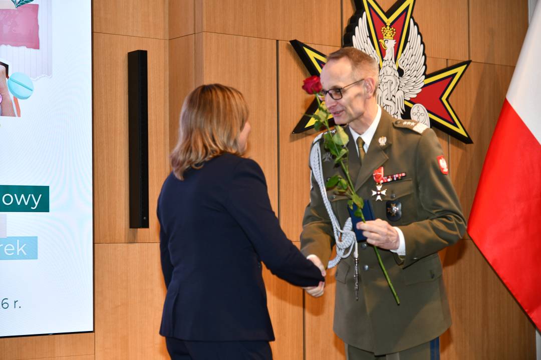 Dyrektor WIM wręcza pielęgniarce czerwoną różę i odznaczenie.