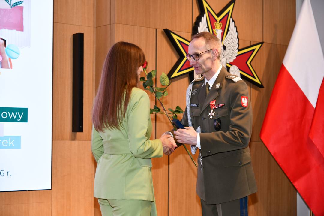 Dyrektor WIM wręcza czerwoną różę pielęgniarce.