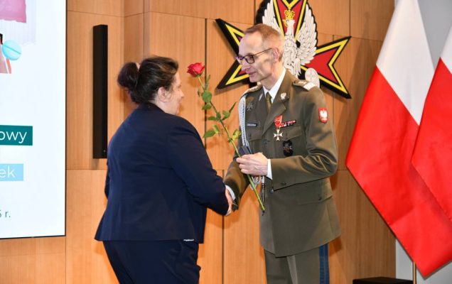 Dyrektor WIM wręcza czerwoną różę pielęgniarce.