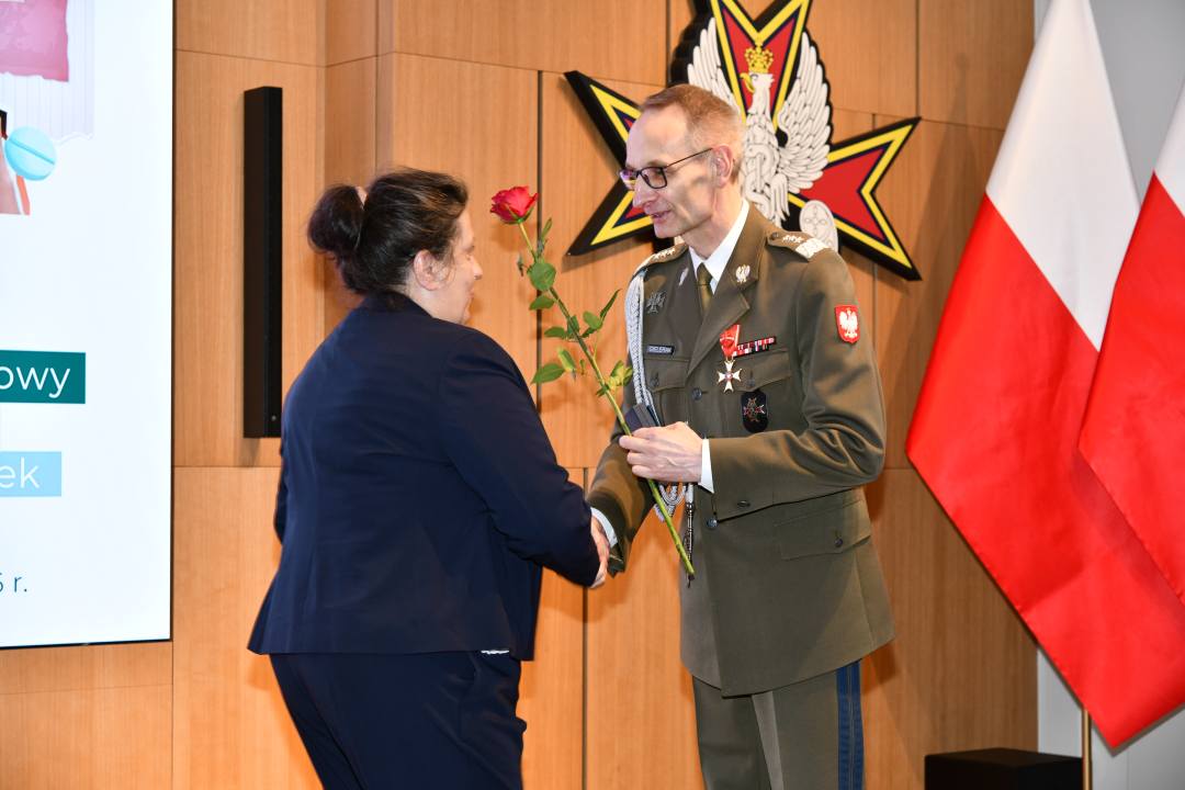 Dyrektor WIM wręcza czerwoną różę pielęgniarce.