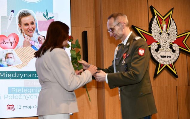 Dyrektor WIM wręcza czerwoną różę pielęgniarce.