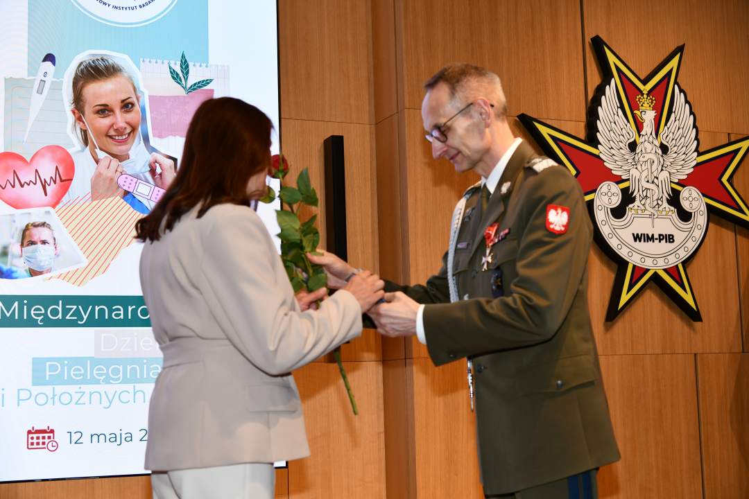 Dyrektor WIM wręcza czerwoną różę pielęgniarce.