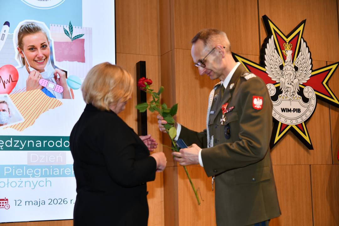 Dyrektor WIM wręcza czerwoną różę pielęgniarce.
