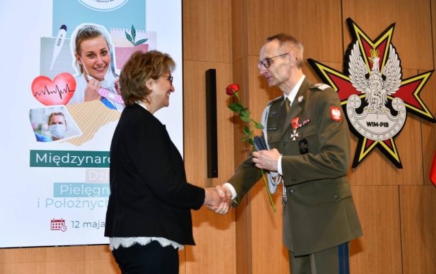 Dyrektor WIM wręcza czerwoną różę pielęgniarce.