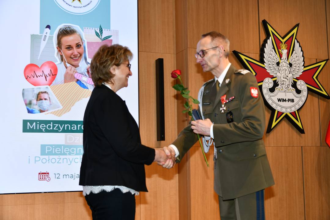 Dyrektor WIM wręcza czerwoną różę pielęgniarce.