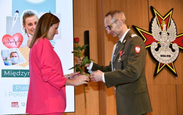 Dyrektor WIM wręcza czerwoną różę pielęgniarce.
