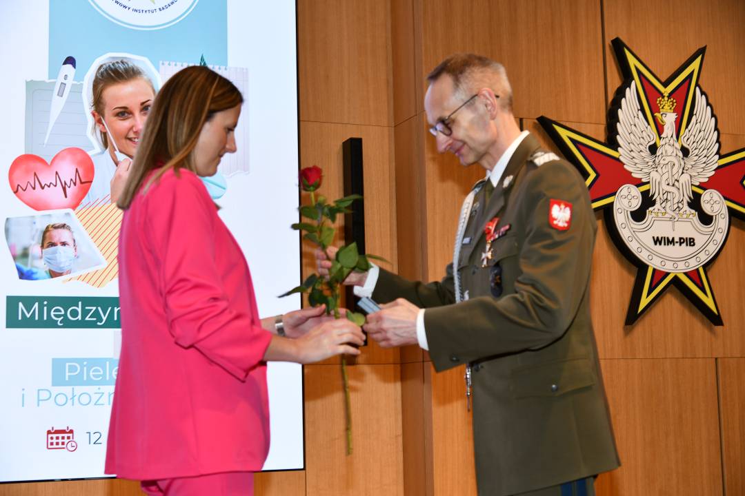 Dyrektor WIM wręcza czerwoną różę pielęgniarce.