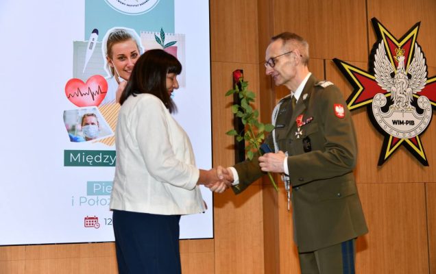 Dyrektor WIM wręcza czerwoną różę pielęgniarce.