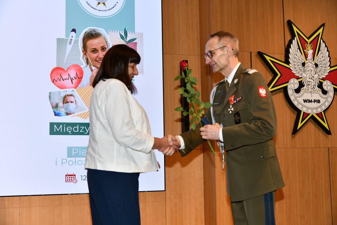 Dyrektor WIM wręcza czerwoną różę pielęgniarce.
