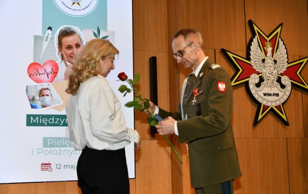 Dyrektor WIM wręcza czerwoną różę pielęgniarce.