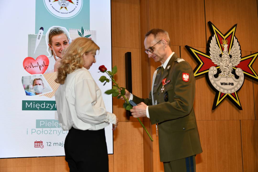 Dyrektor WIM wręcza czerwoną różę pielęgniarce.