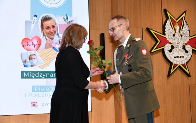 Dyrektor WIM wręcza czerwoną różę pielęgniarce.