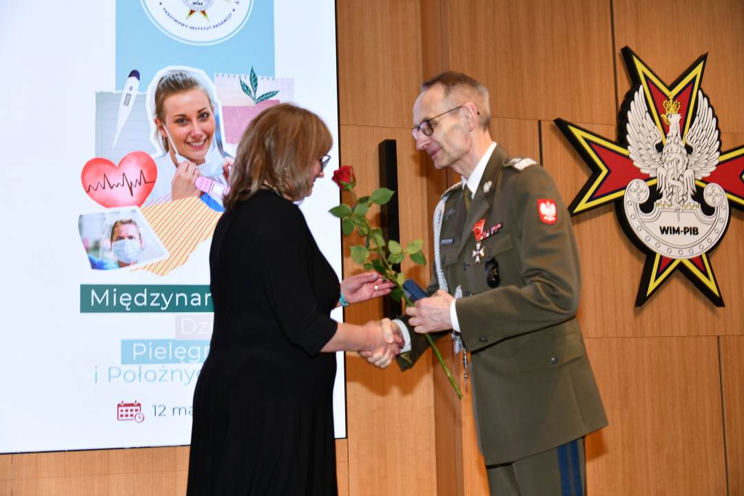Dyrektor WIM wręcza czerwoną różę pielęgniarce.