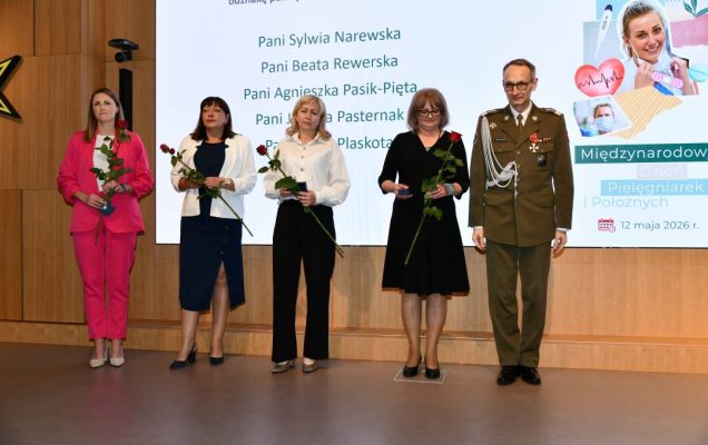 Dyrektor WIM i pielęgniarki trzymajce czerwone róże i odznaczenia pozują do wspólnego zdjęcia.
