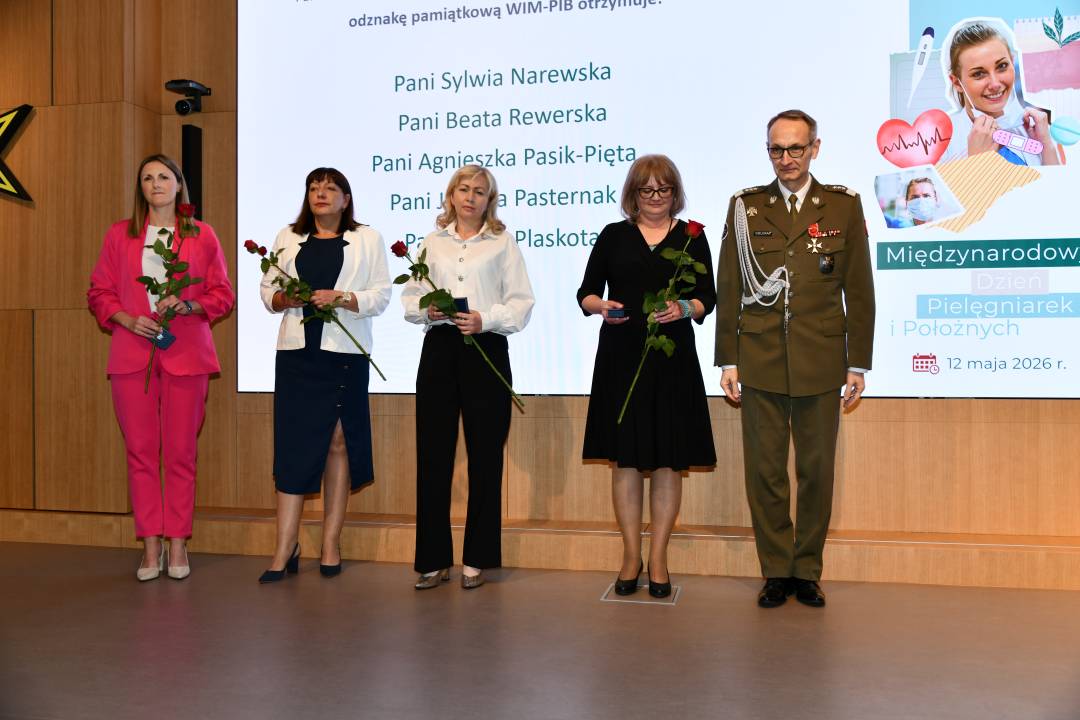 Dyrektor WIM i pielęgniarki trzymajce czerwone róże i odznaczenia pozują do wspólnego zdjęcia.