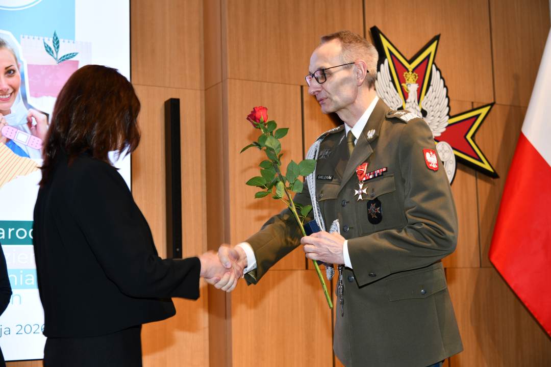 Dyrektor WIM wręcza czerwoną różę pielęgniarce.