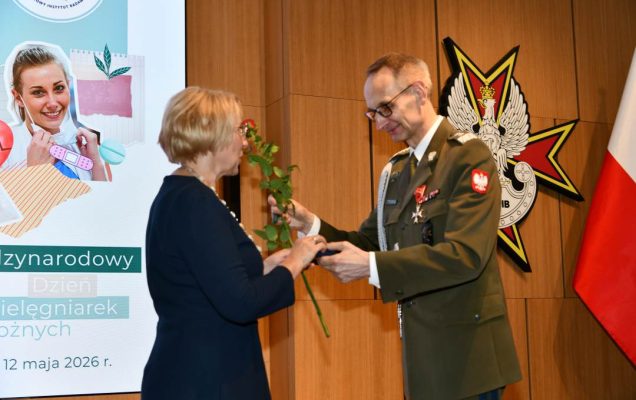 Dyrektor WIM wręcza czerwoną różę pielęgniarce.