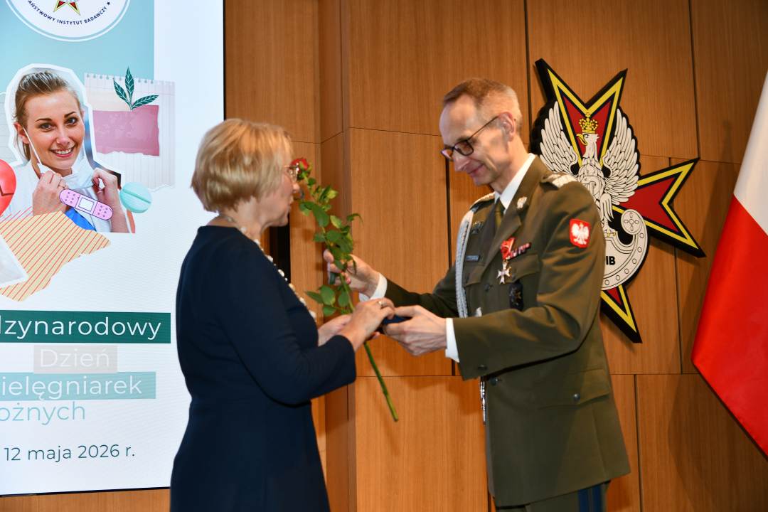 Dyrektor WIM wręcza czerwoną różę pielęgniarce.
