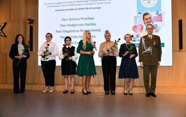 Dyrektor WIM z pielęgniarkami trzymającymi odznaczenia i czerwone róże pozują do zdjęcia.