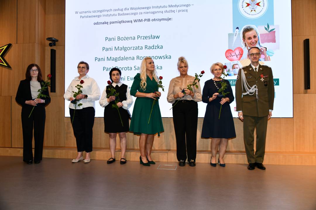 Dyrektor WIM z pielęgniarkami trzymającymi odznaczenia i czerwone róże pozują do zdjęcia.