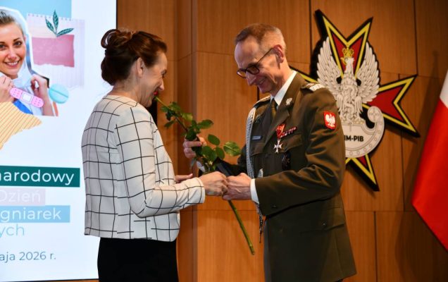 Dyrektor WIM wręcza czerwoną różę pielęgniarce.