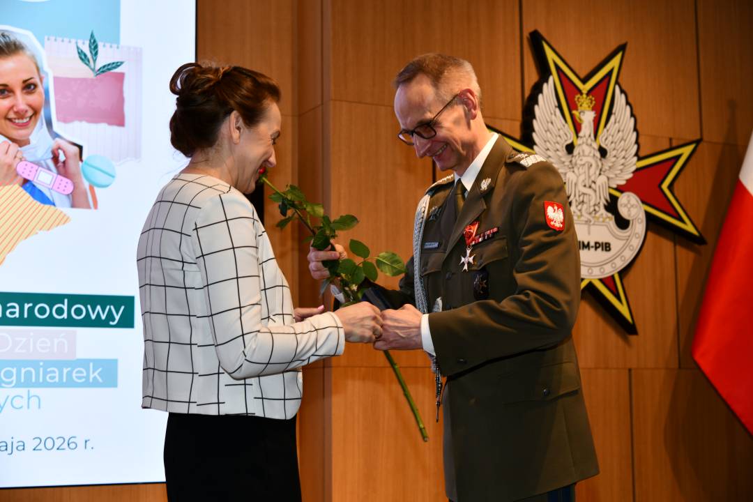 Dyrektor WIM wręcza czerwoną różę pielęgniarce.