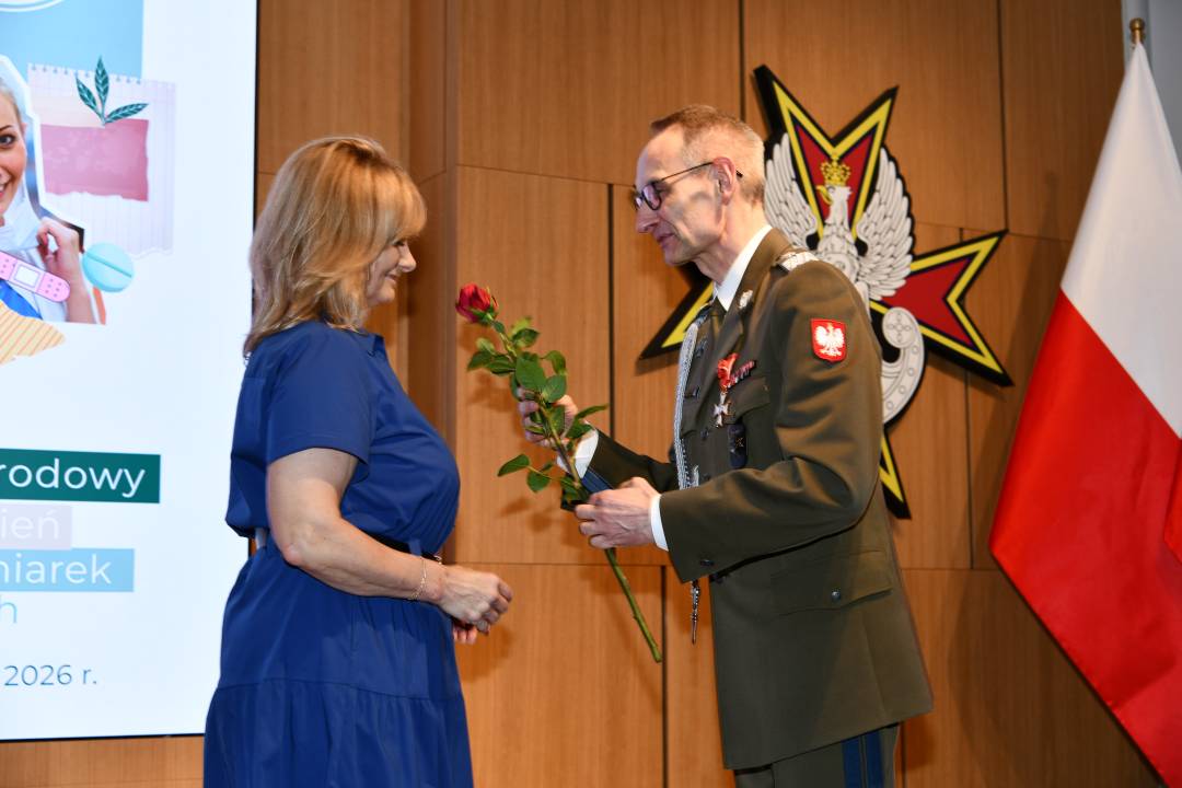 Dyrektor WIM wręcza czerwoną różę pielęgniarce.