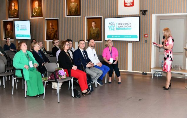Małgorzata Złotkowska, kierownik Biura Dyrektora WIM-PIB, główny specjalista ds. komunikacji wewnętrznej prowadzi konferencję. Przed nią siedzący uczestnicy konferencji.