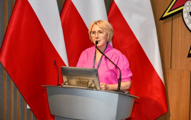 Agata Stępniak przy mównicy, za jej plecami 3 flagi Polski.