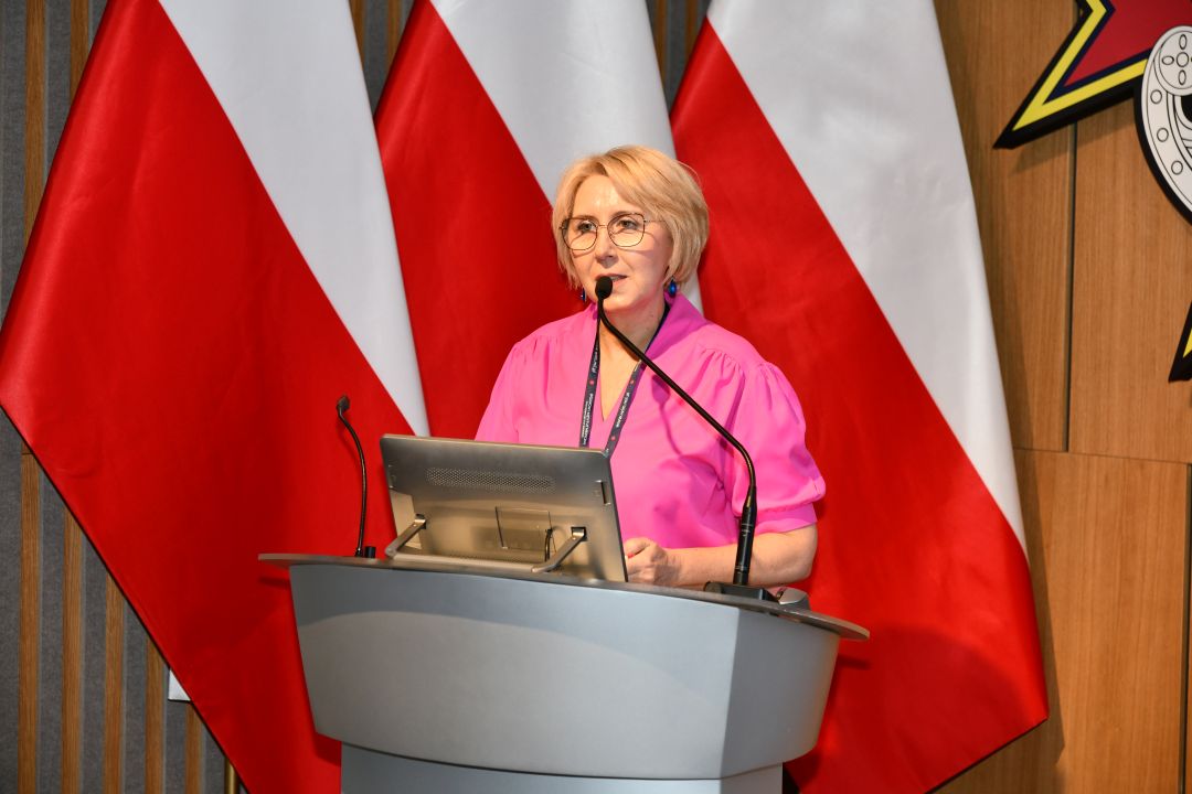 Agata Stępniak przy mównicy, za jej plecami 3 flagi Polski.