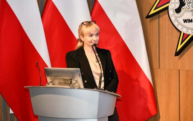 Prelegentka przy mównicy w sali Wojskowego Instytutu Medycznego; obok polska flaga i emblemat WIM‑PIB.