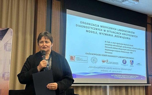 Kierownik Zakładu Diagnostyki Laboratoryjnej dr hab. n. med. Agnieszka Woźniak-Kosek z mikrofonem w ręku na sali konferencyjnej za nią na dużym ekranie wyświetlony slajd z prezentacji.