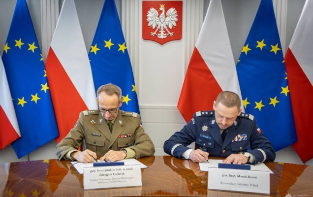 Grzegorz Gielerak i Roman Smogorzewski podpisują przy stole listy intencyjne. Za ich plecami godło RP oraz flagi UE i RP.