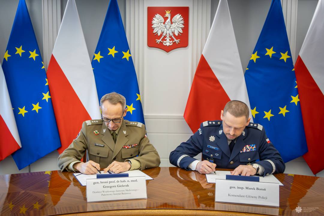 Grzegorz Gielerak i Roman Smogorzewski podpisują przy stole listy intencyjne. Za ich plecami godło RP oraz flagi UE i RP.