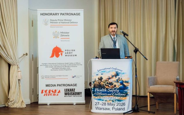 Józef Mróz przy mównicy, za nim plakat konferencji.