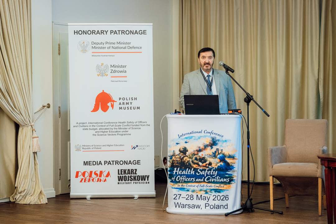 Józef Mróz przy mównicy, za nim plakat konferencji.
