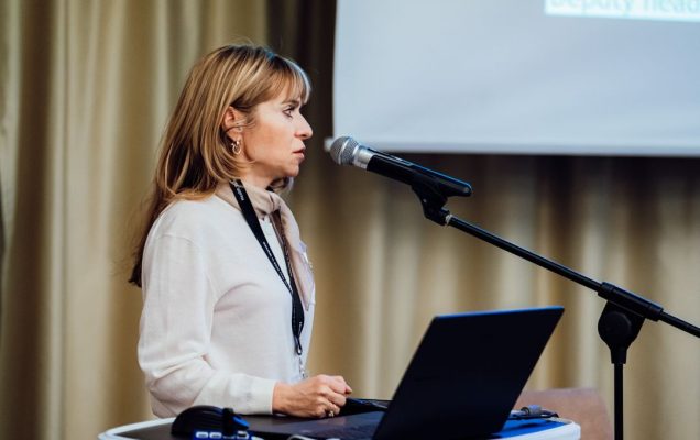 Katarzyna Gniadek przy mównicy, za nią ekran z wyświetlonym slajdem prezentacji.