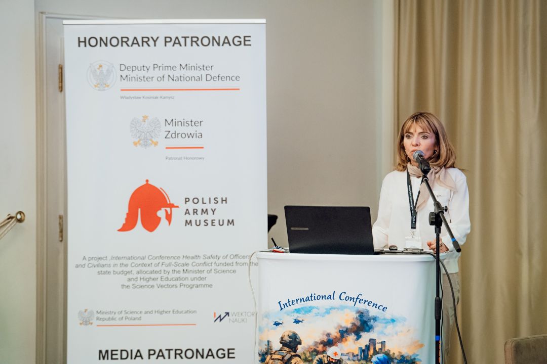 Katarzyna Gniadek przy mównicy, obok niej stoi plakat konferencyjny.