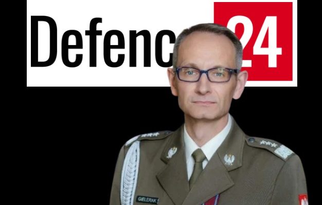Grzegorz Gilerak, za nim logo defence24.