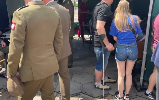 Weteran podpierający się kulą, młoda kobieta, żołnierze oglądają stoisko Centrum Leczenia Weterana WIM.
