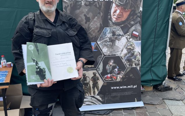 Żołnierz przy punkcie namiocie wystawienniczym Centrum Leczenia Weterana prezentuje okolicznościową książkę z dedykacją na jednej ze stron książki.