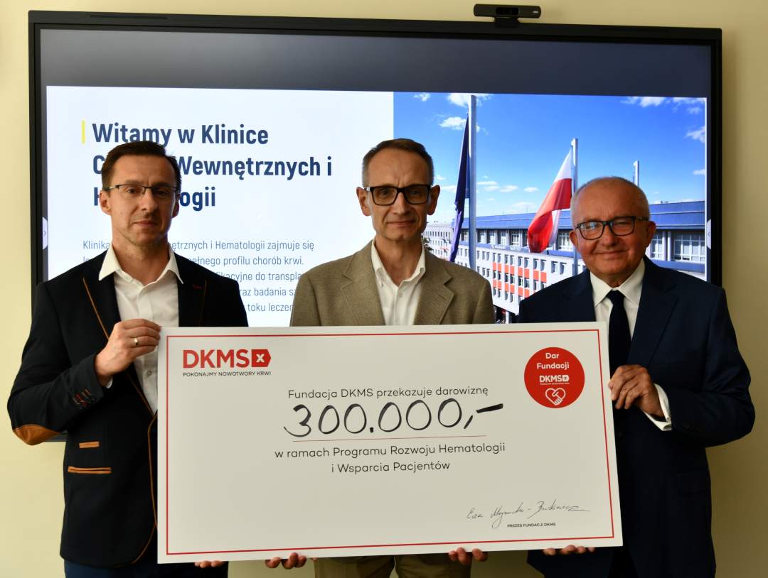 Dyrektor WIM-PIB, prof. Piotr Rzepecki i przedstawicie; Fundacji DKMS prezentują duży czek z wypisaną kwotą.