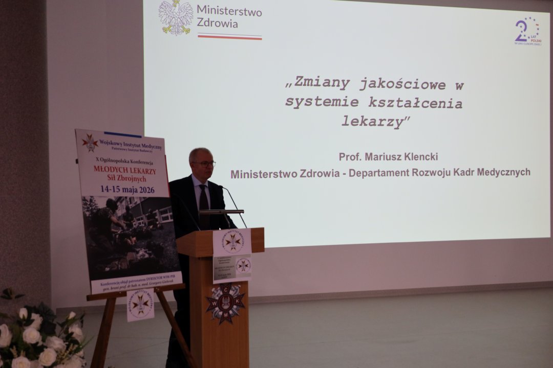 Prof. Mariusz Klencki przy mównicy za jego plecami wyświetlony slajd prezentacji: Zmiany jakościowe w systemie kształcenia lekarzy.