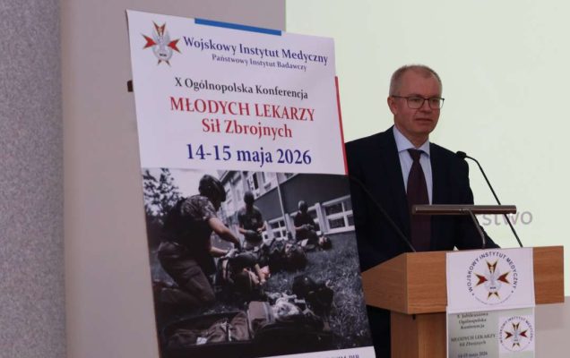 Prelegent przy mównicy, obok niego na stojaku plakat 10. konferencji Młodych Lekarzy, 14-15 maja 2026.