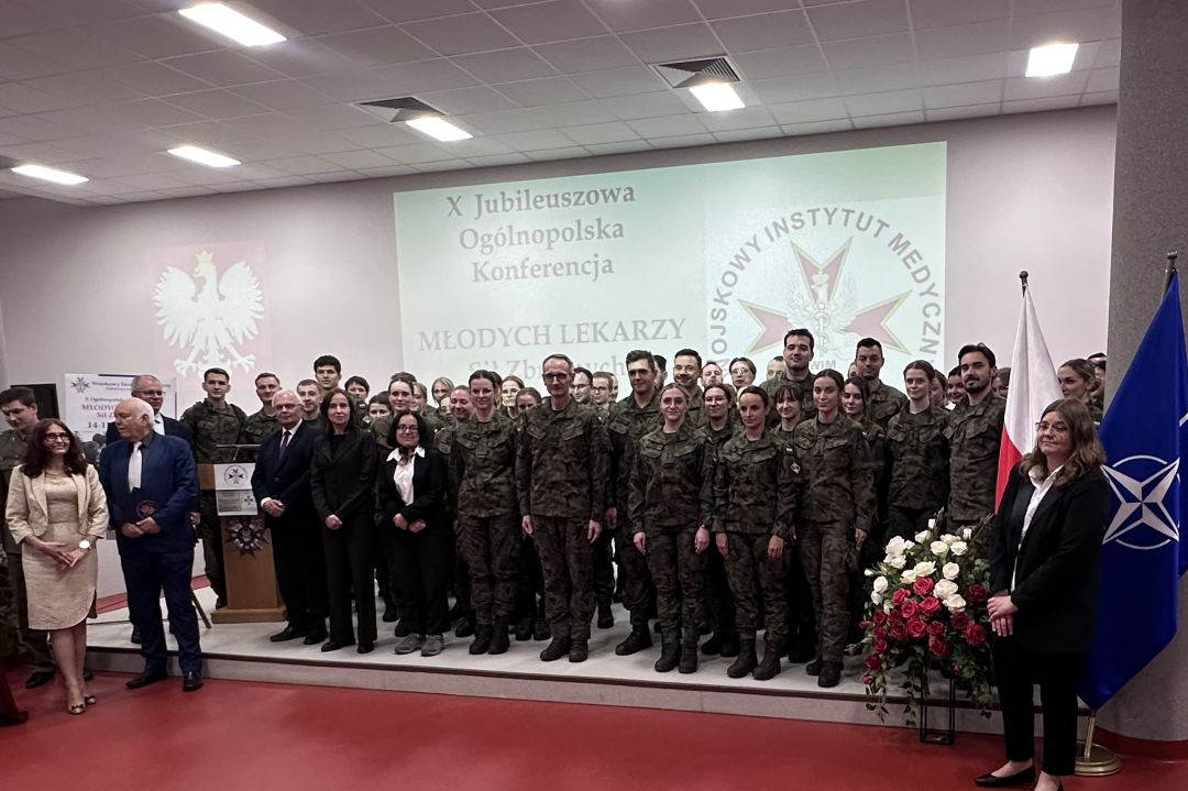 Zdjęcie grupowe uczestników konferencji, za nimi wyświetlony slajd z nazwą konferencji i logo WIM.
