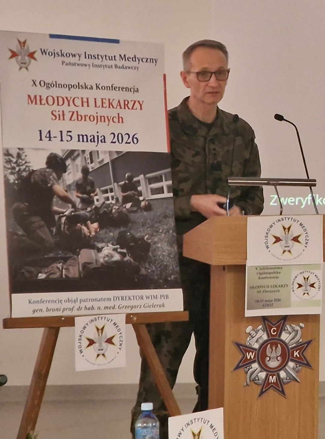 Dyrektor WIM przy mównicy, obok niego plakat konferencji,