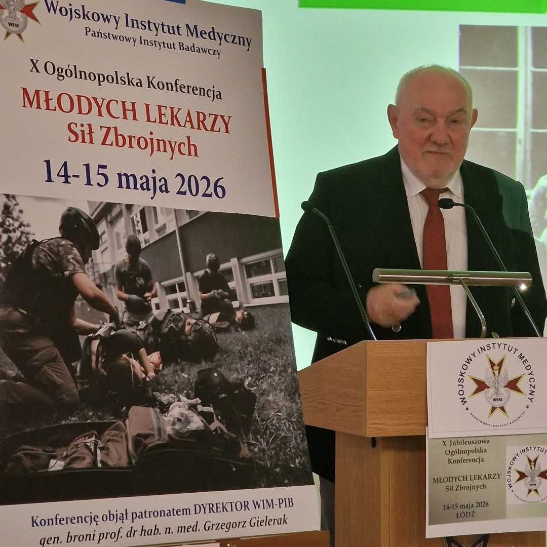 Prelegent przy mównicy, obok niego plakat konferencji,