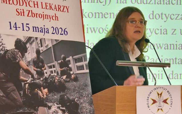 Agnieszka Wyrwas przy mównicy. Obok niej plakat konferencyjny, za jej plecami na wielkim ekranie wyświetlony slajd z prezentacji.
