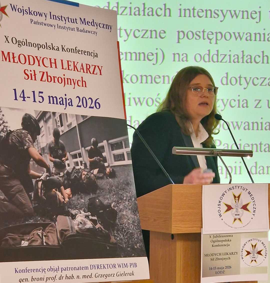 Agnieszka Wyrwas przy mównicy. Obok niej plakat konferencyjny, za jej plecami na wielkim ekranie wyświetlony slajd z prezentacji.